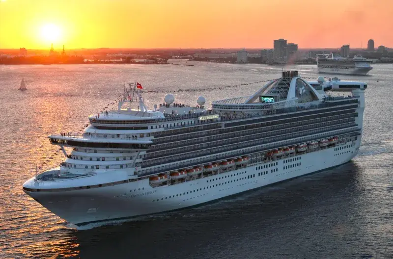 Caribbean Princess'in gün batımında şehir önünde seyri; güvertede bayrak süslemeleri