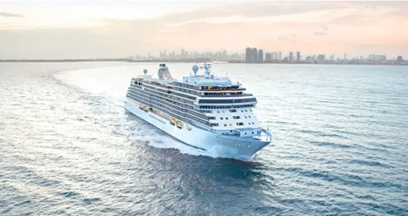 Seven Seas Splendor açık denizde, arkada şehir silueti